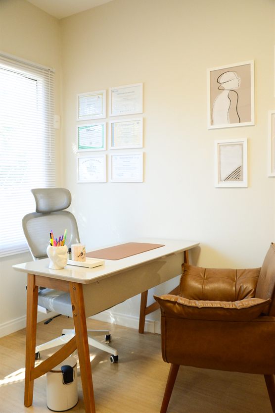 A sala de atendimento: a mesa junto à janela, os diplomas na parede e a poltrona.